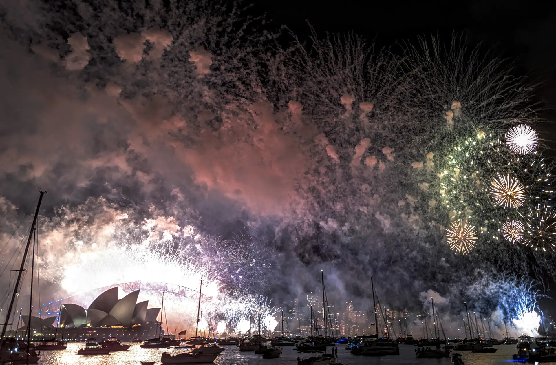 Midnight fireworks and smoke over Sydney Harbour, with the Opera House lit up and boats on the water