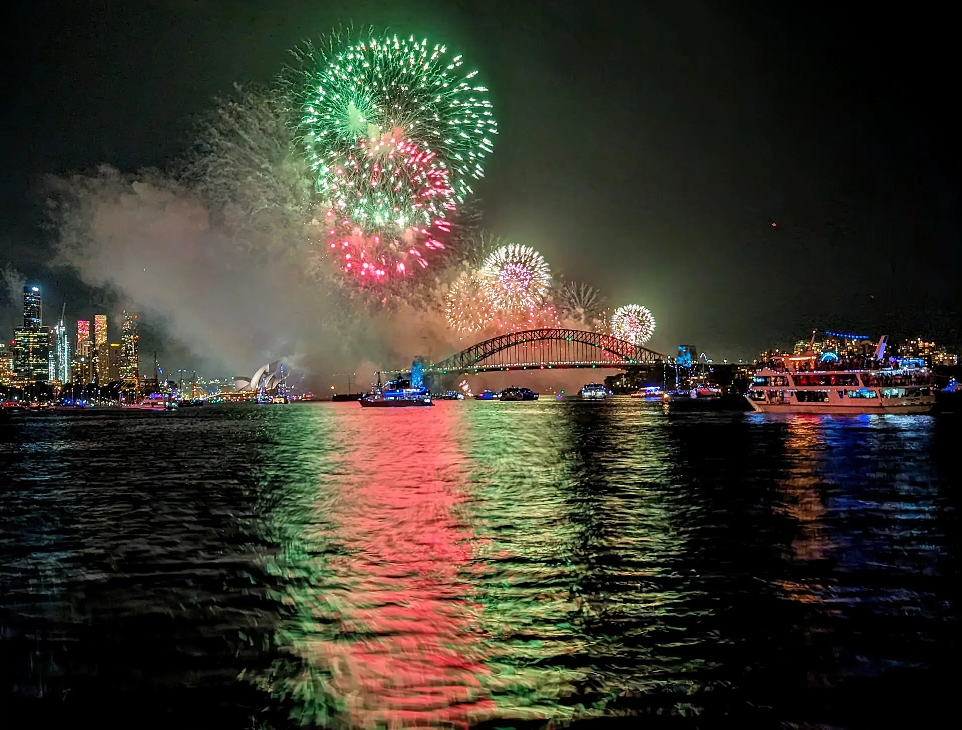 Fireworks over the Harbour Bridge reflected in the water, with cruise boats on the harbour
